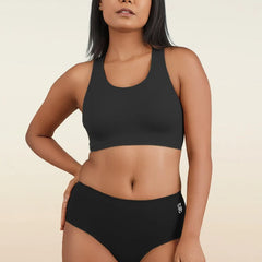 Woman wearing a black sports bra and mid-waist underwear on a beige background