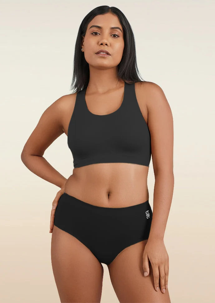 Woman wearing a black sports bra and mid-waist underwear on a beige background