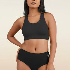 Woman wearing a black sports bra and mid-waist underwear on a beige background
