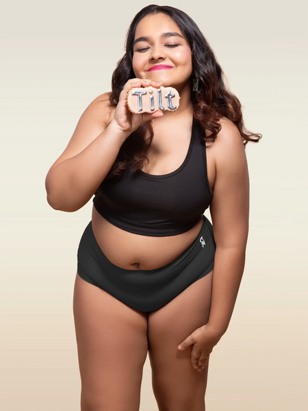 Woman wearing a black underwear holding a 'Tilt' sign against a beige background