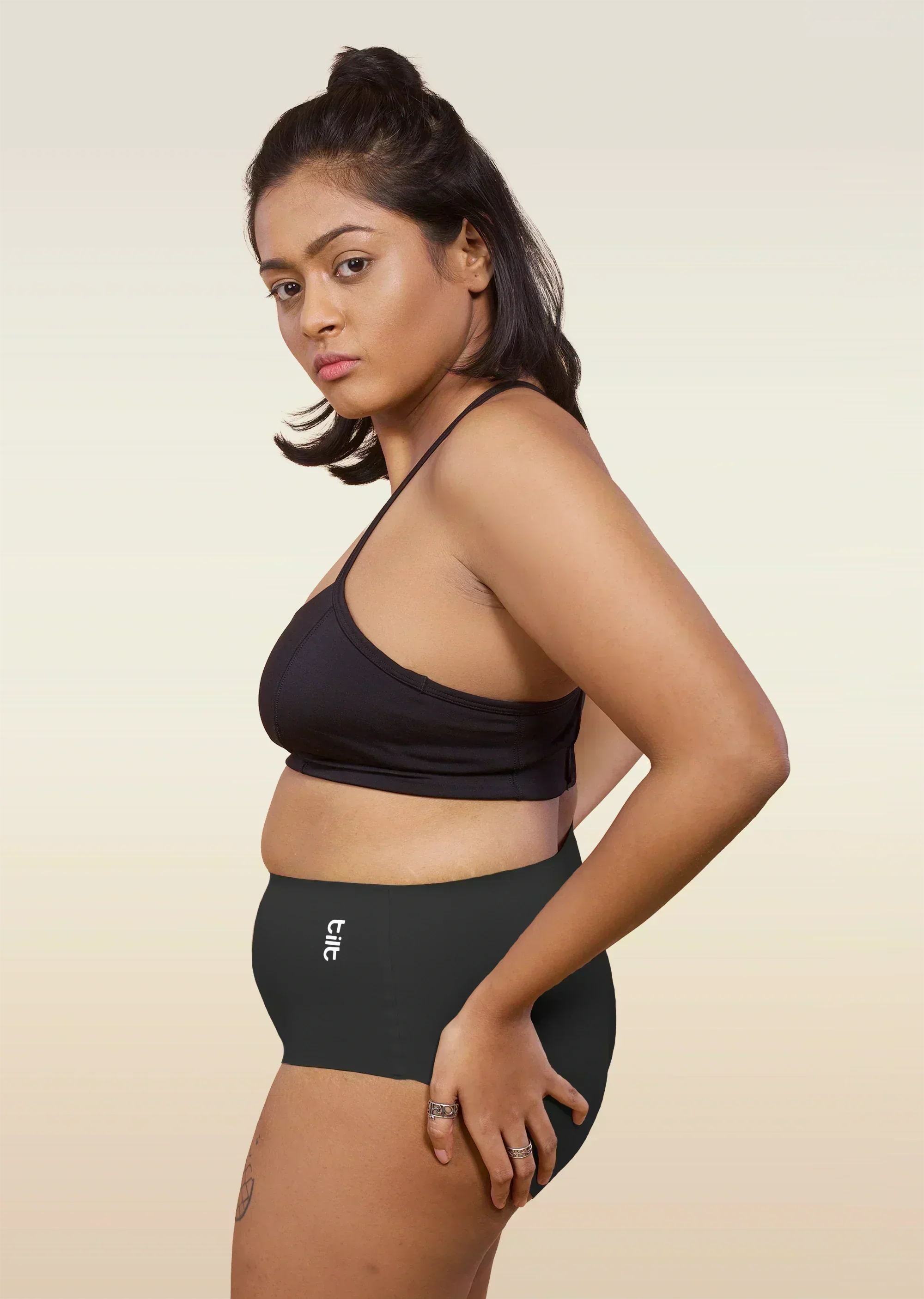 Woman wearing a black bra and  black mid-waist underwear with a beige background