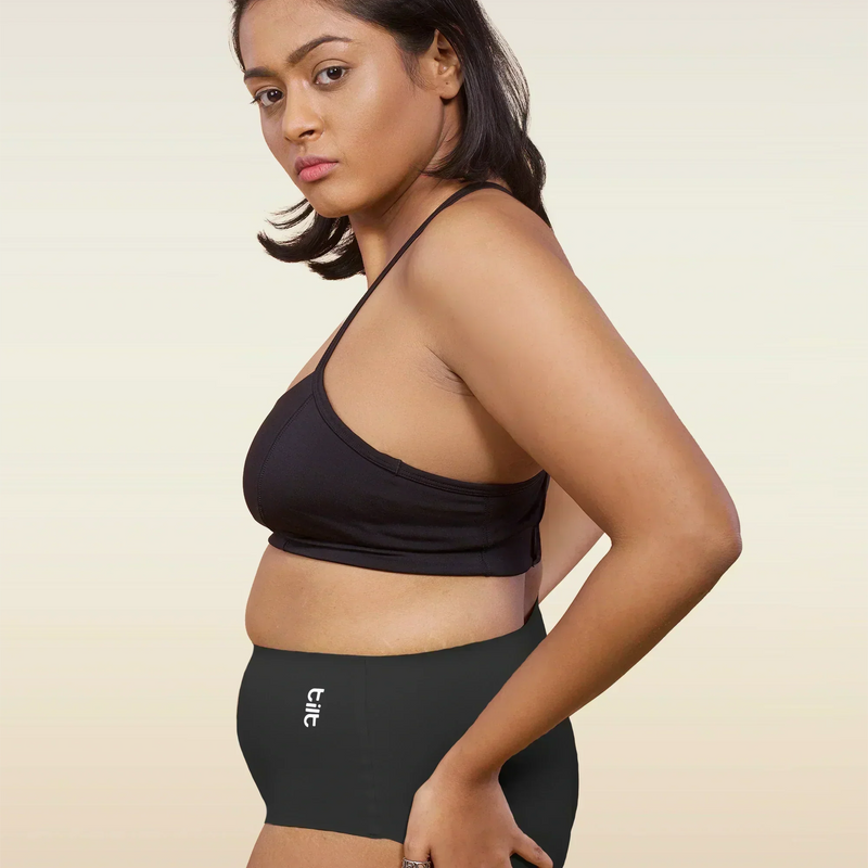 Woman wearing a black bra and  black mid-waist underwear with a beige background