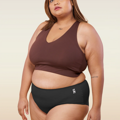 Woman wearing a brown sports bra and black mid-waist underwear on a beige background