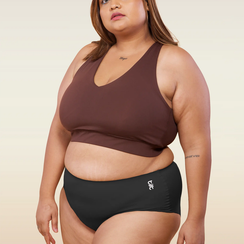 Woman wearing a brown sports bra and black mid-waist underwear on a beige background