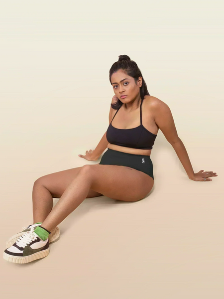 Woman wearing a black sports bra and underwear sitting on a beige background