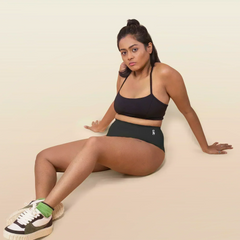 Woman wearing a black sports bra and underwear sitting on a beige background