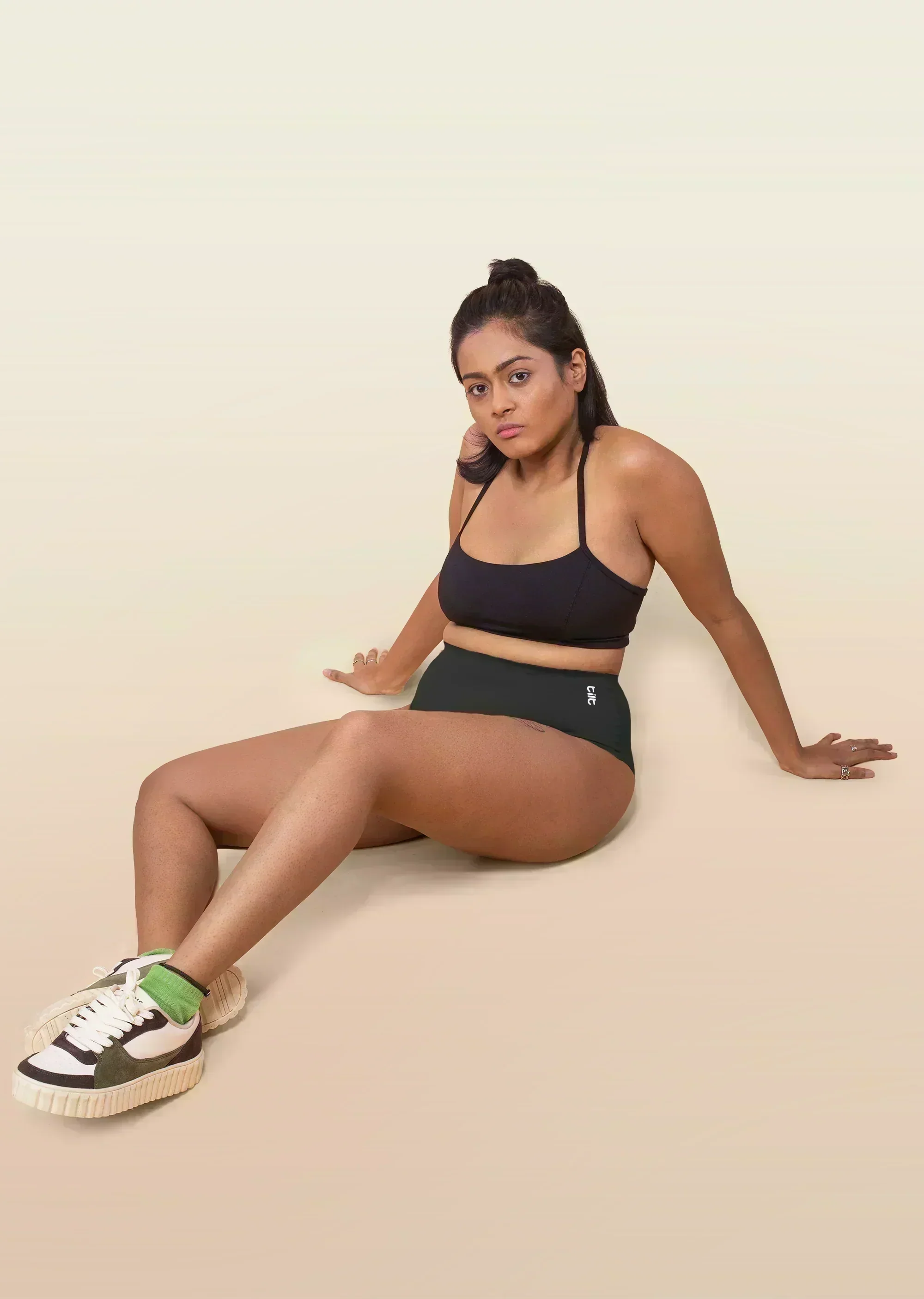 Woman wearing a black sports bra and underwear sitting on a beige background
