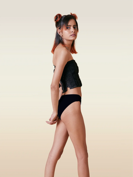 Woman wearing a black top and underwear on a beige background