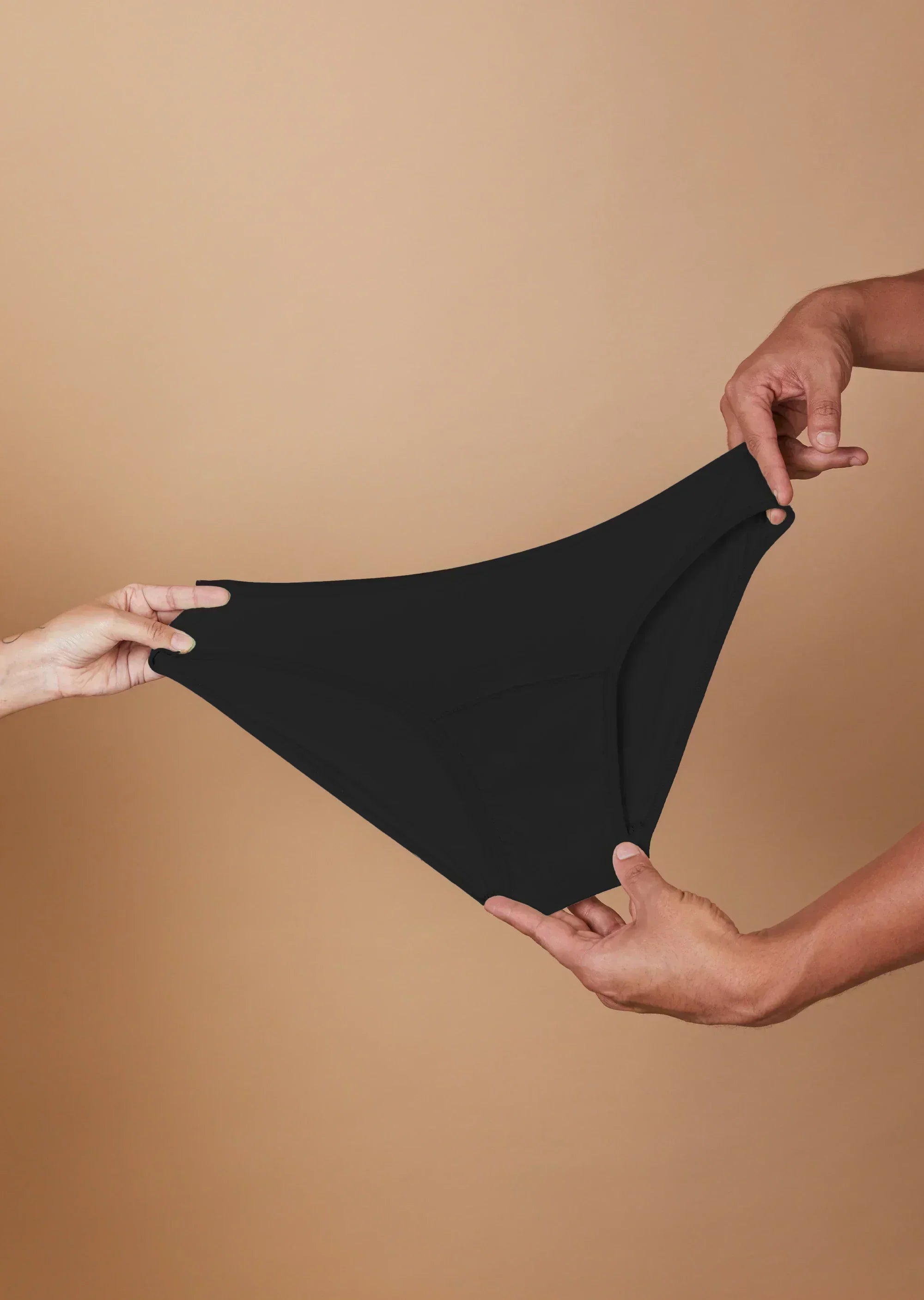Black underwear held between two hands against a beige background