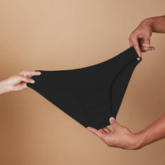 Black underwear held between two hands against a beige background