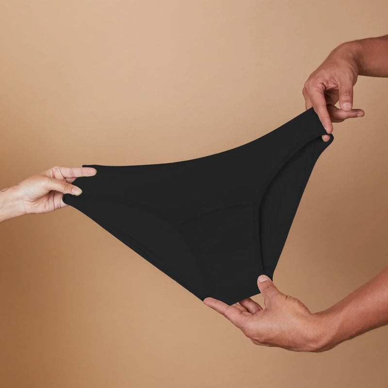 Black underwear held between two hands against a beige background
