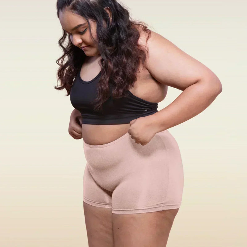 Woman wearing a black sports bra and beige boyshorts on a plain background