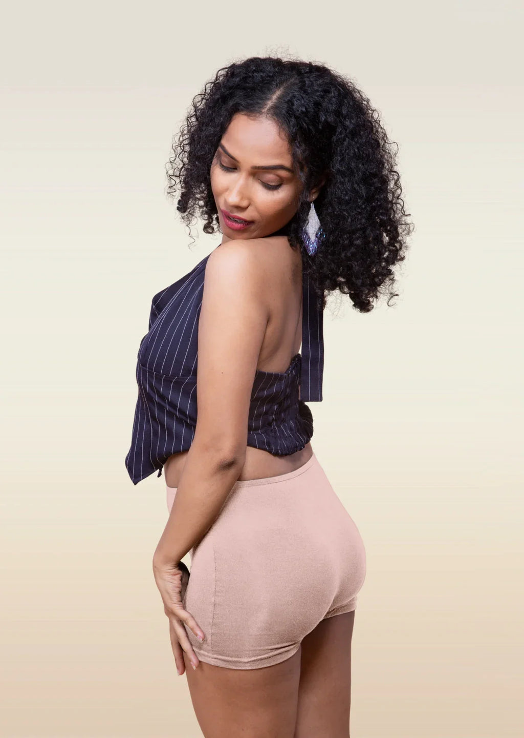 Woman wearing a striped top and beige  boyshorts against a beige background