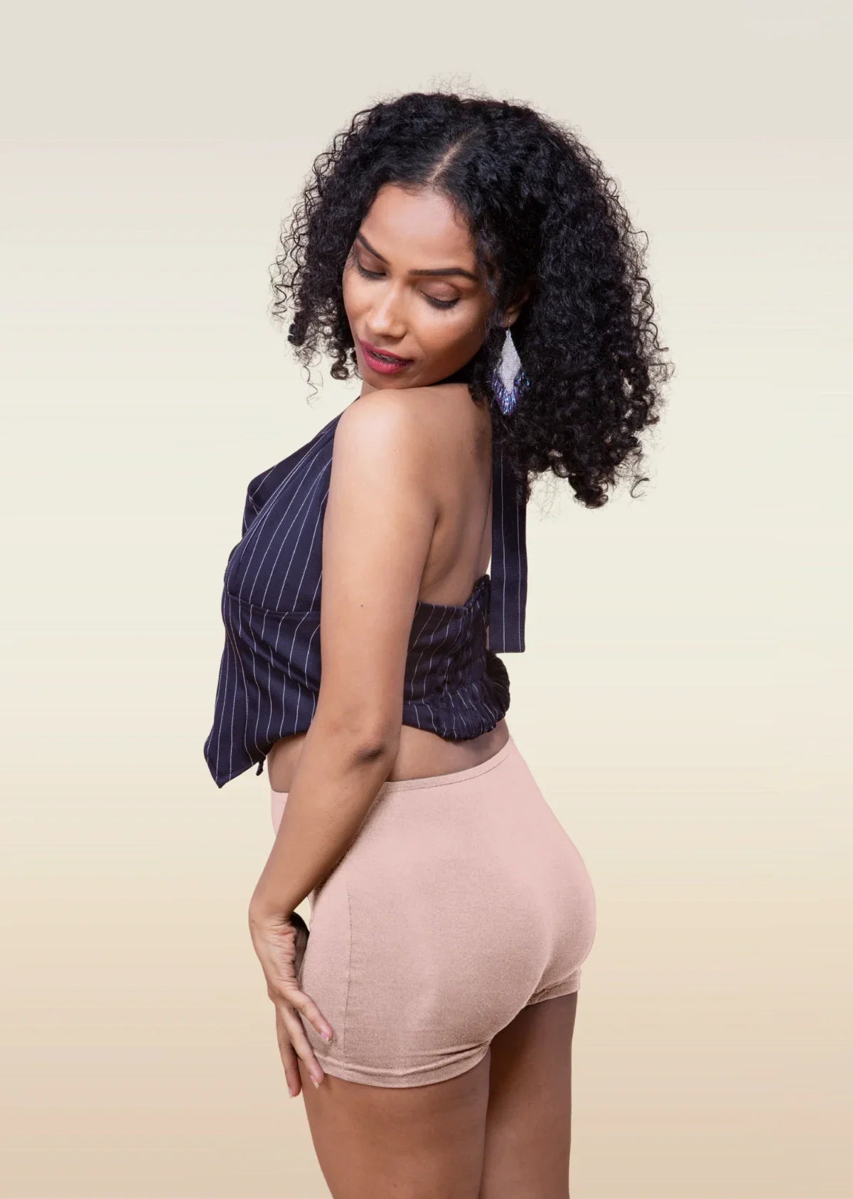 Woman wearing a striped top and beige  boyshorts against a beige background