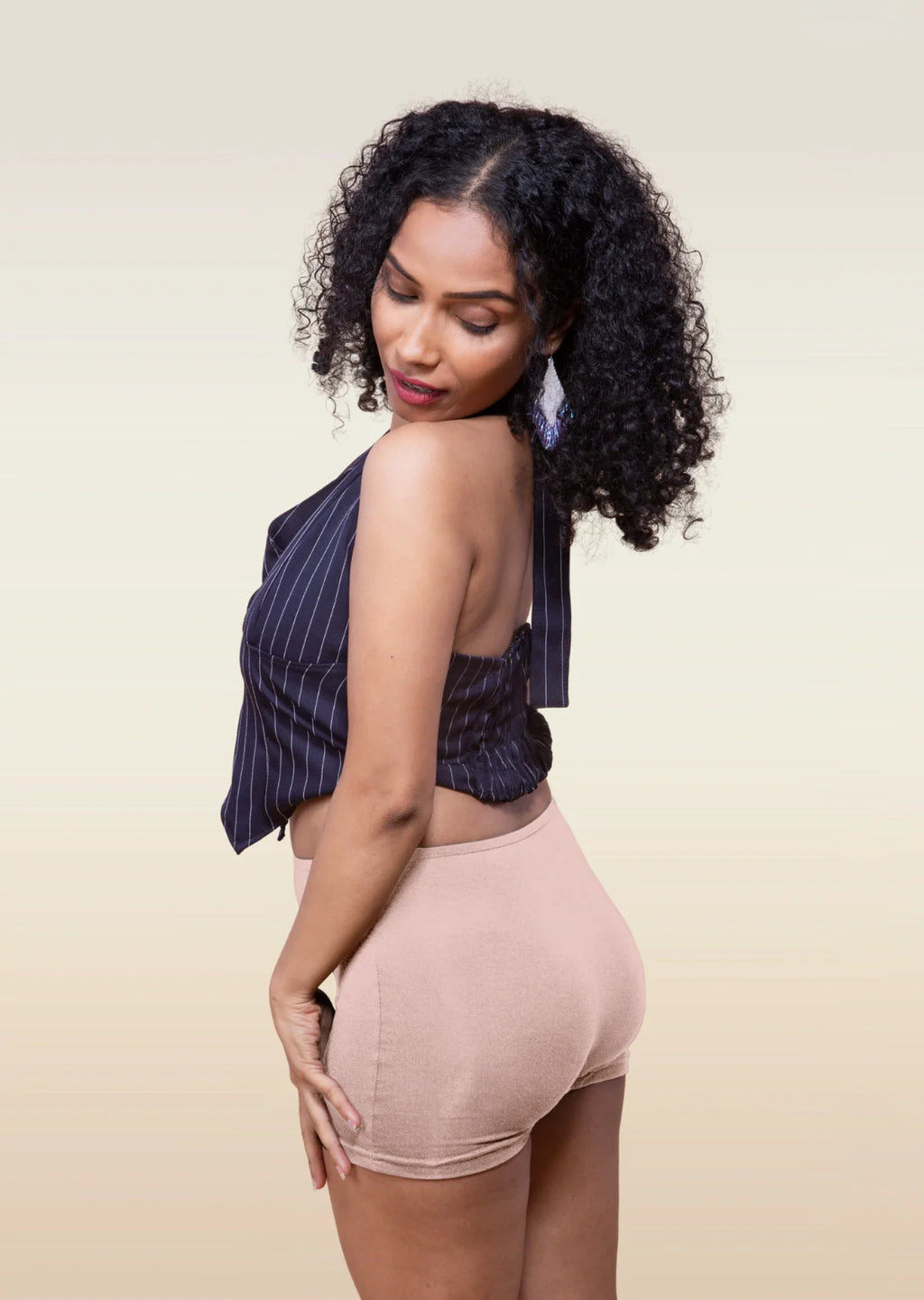 Woman wearing a striped top and beige  boyshorts against a beige background