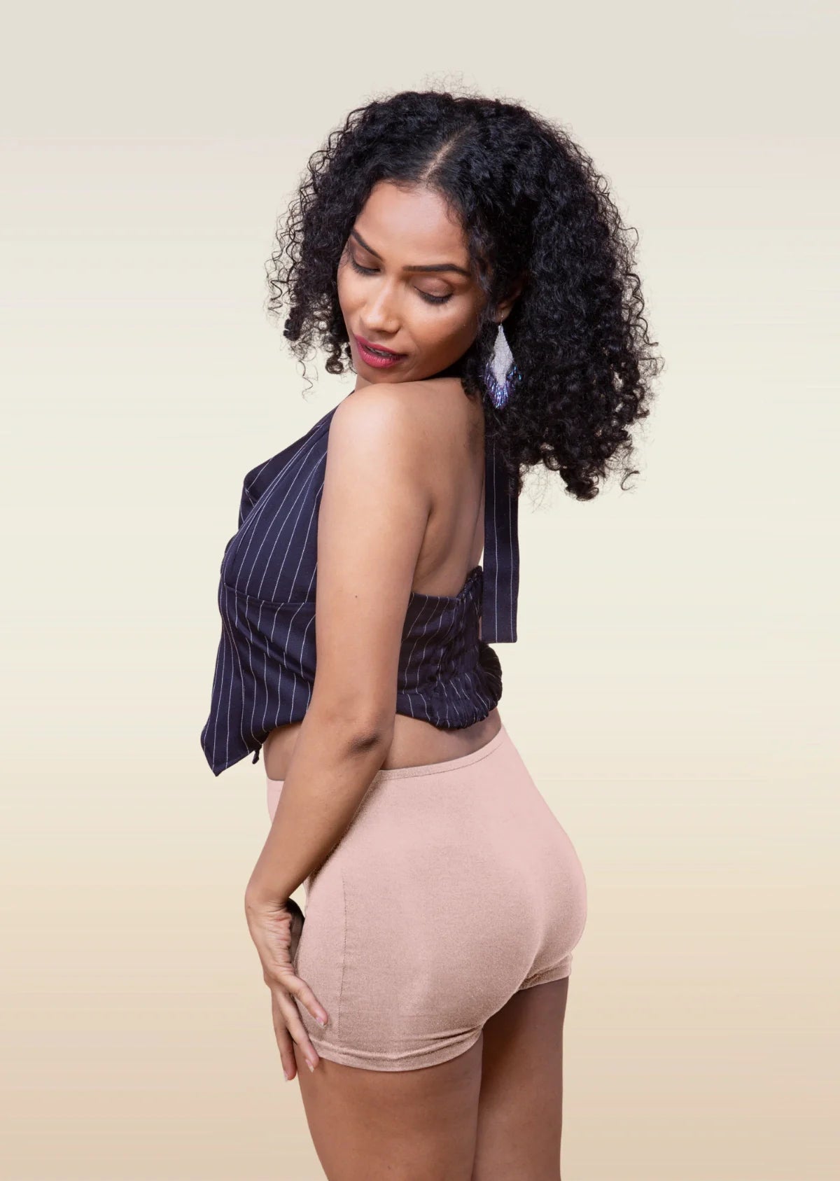 Woman wearing a striped top and beige  boyshorts against a beige background