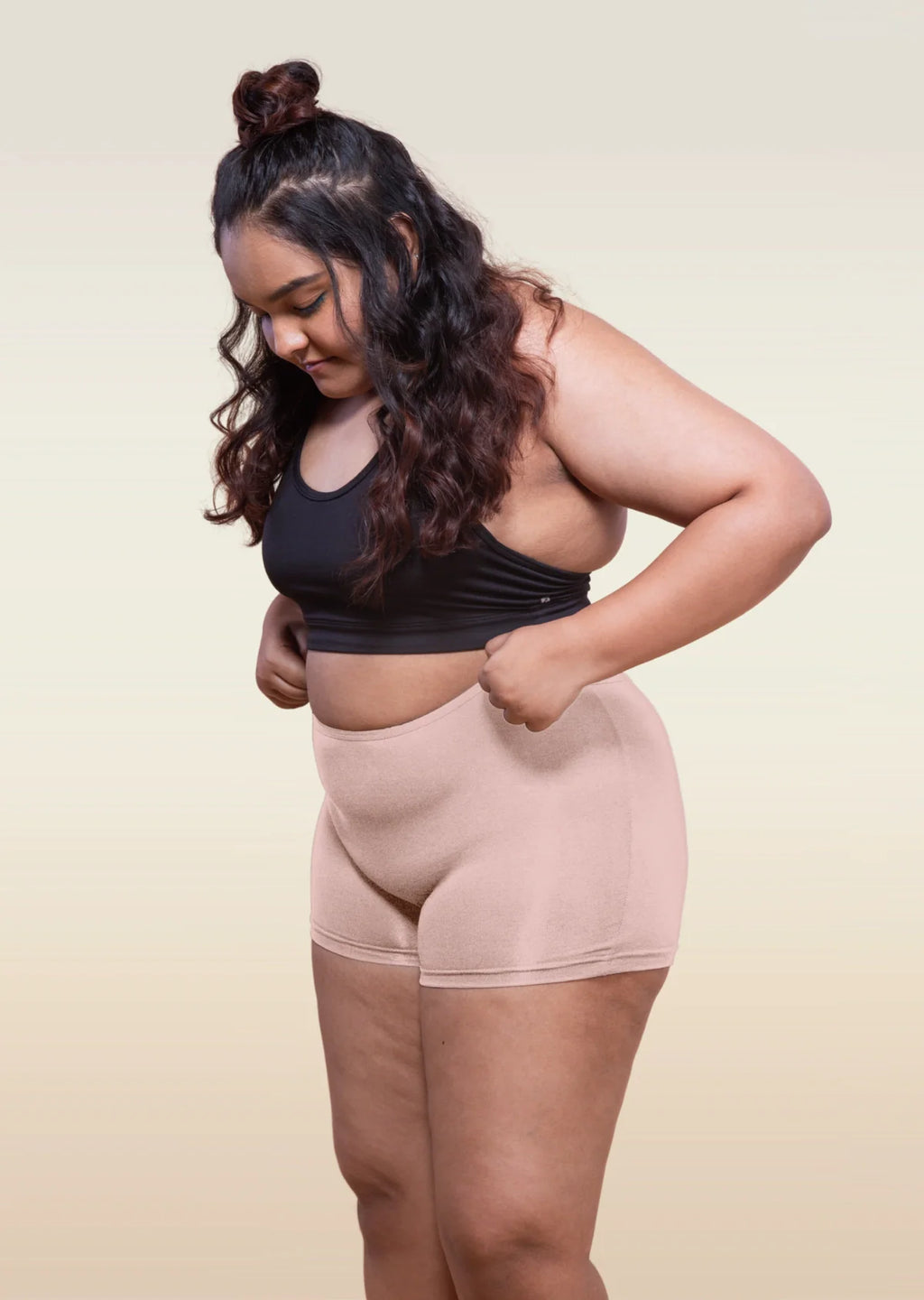 Woman wearing a black sports bra and beige boyshorts on a plain background