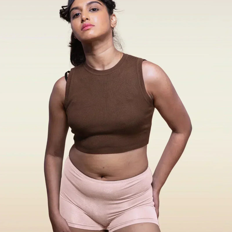 Woman wearing a brown sleeveless top and beige boyshorts against a beige background