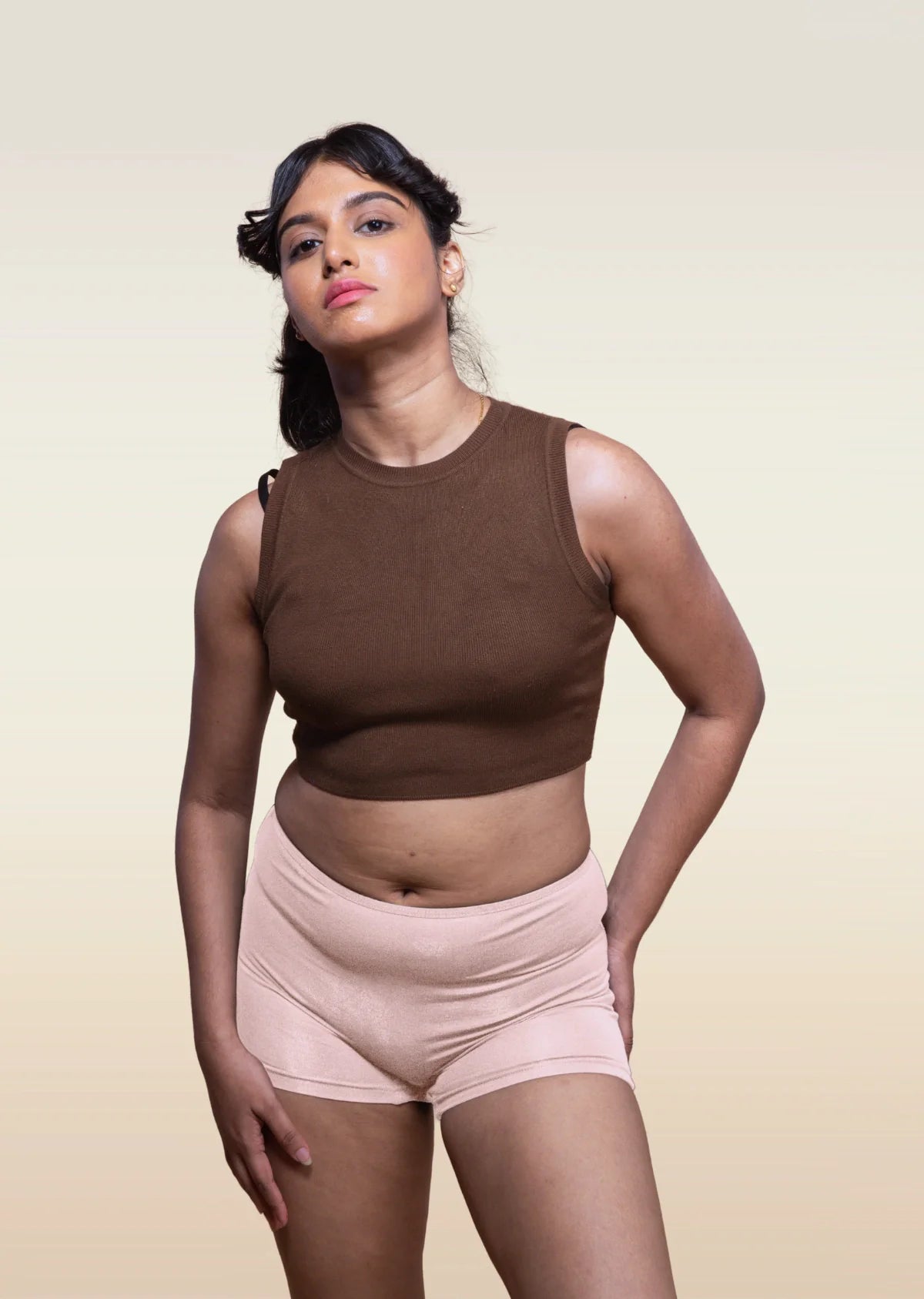 Woman wearing a brown sleeveless top and beige boyshorts against a beige background
