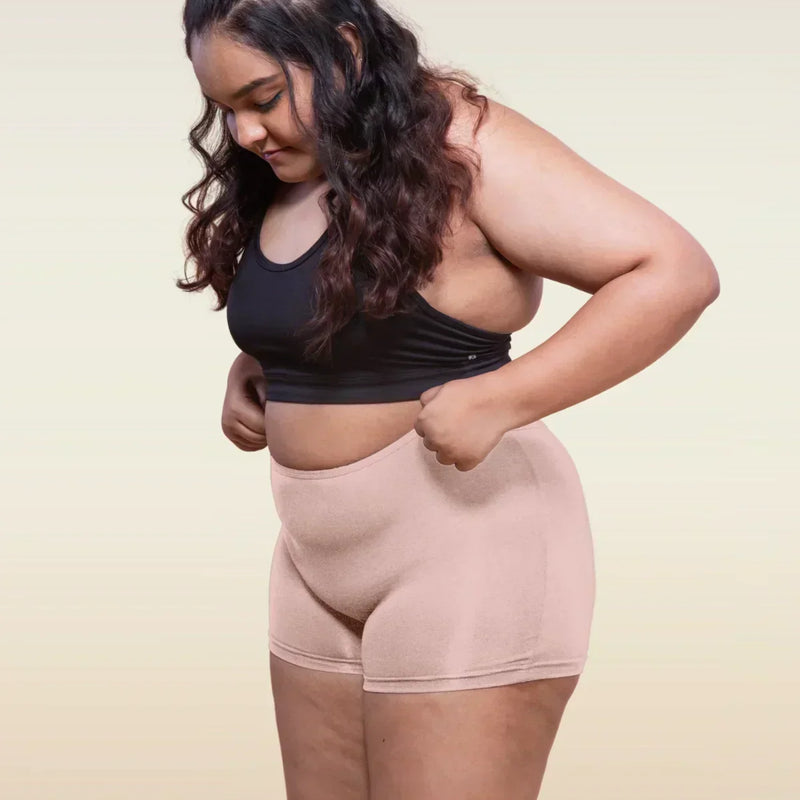Woman wearing a black sports bra and beige boyshorts on a plain background