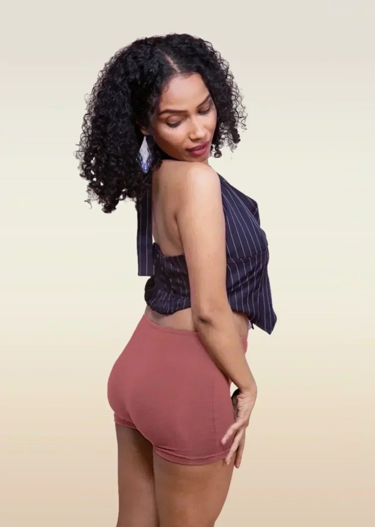 Woman wearing a striped top and red boyshorts against a beige background