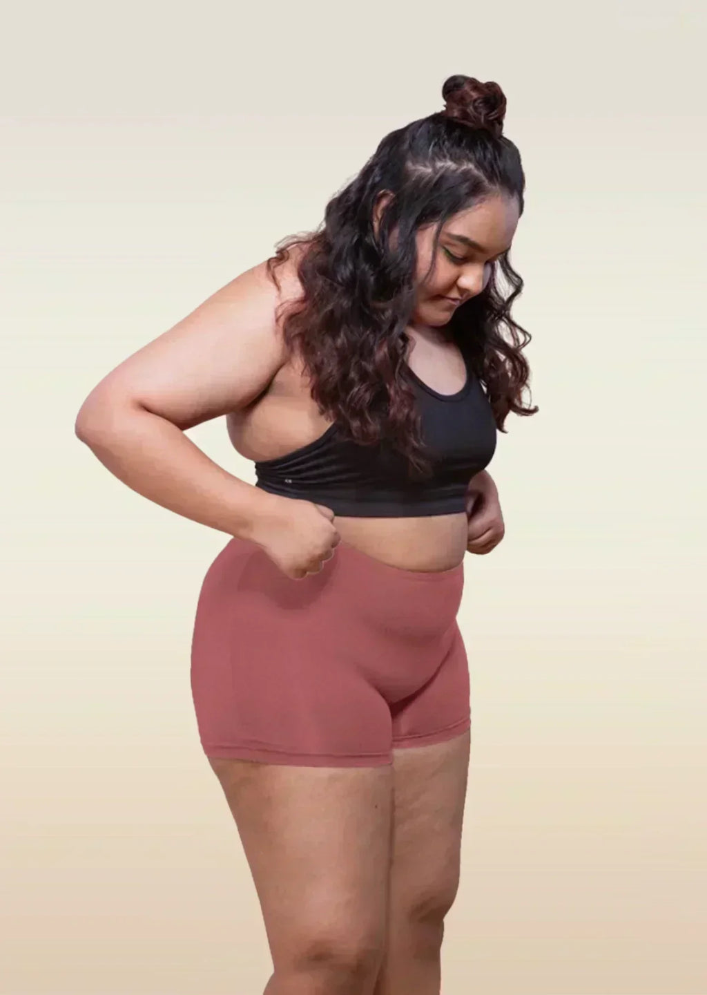 Woman wearing a black sports bra and red boyshorts on a beige background