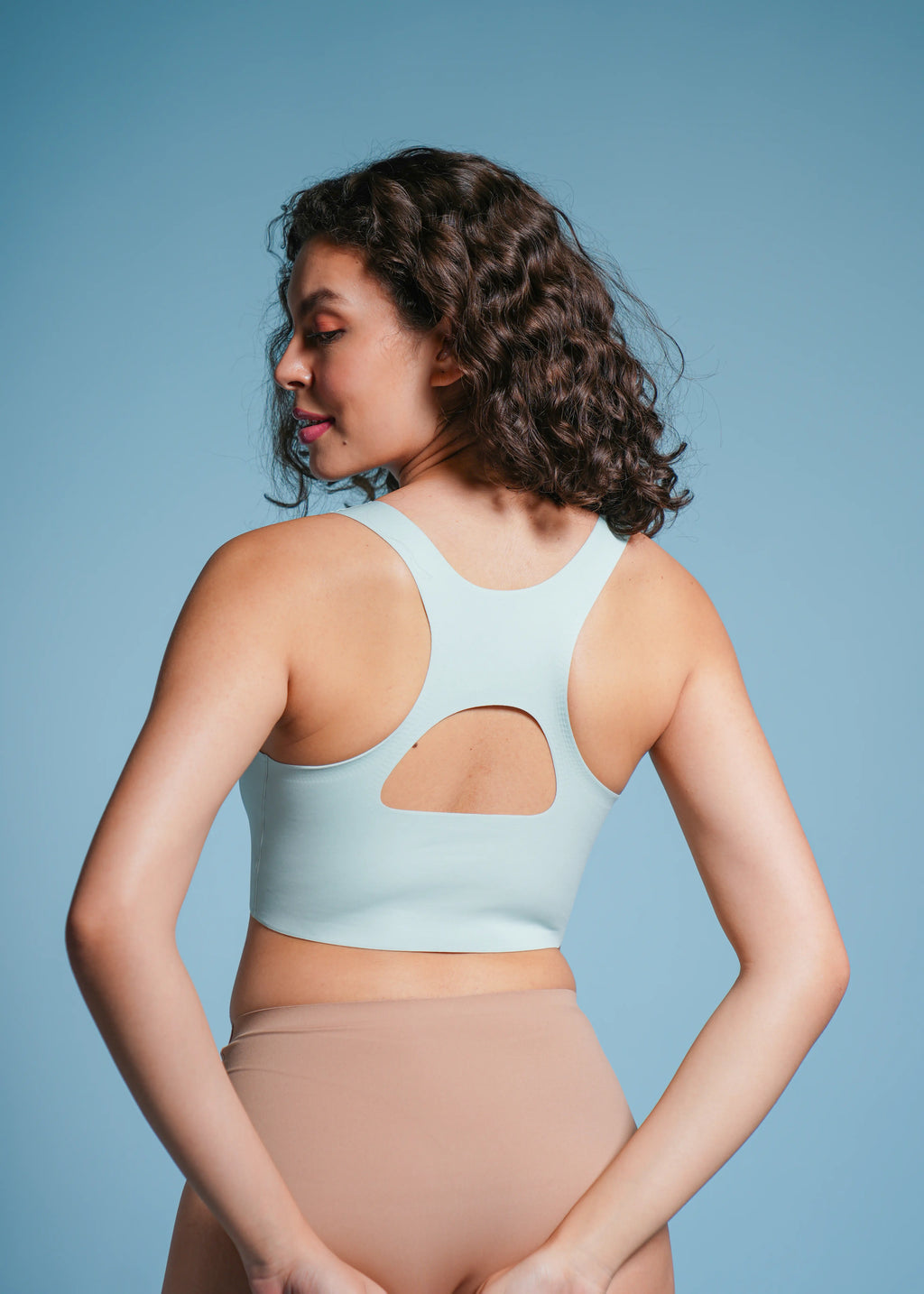 Woman wearing a light blue bra and beige underwear against a blue background