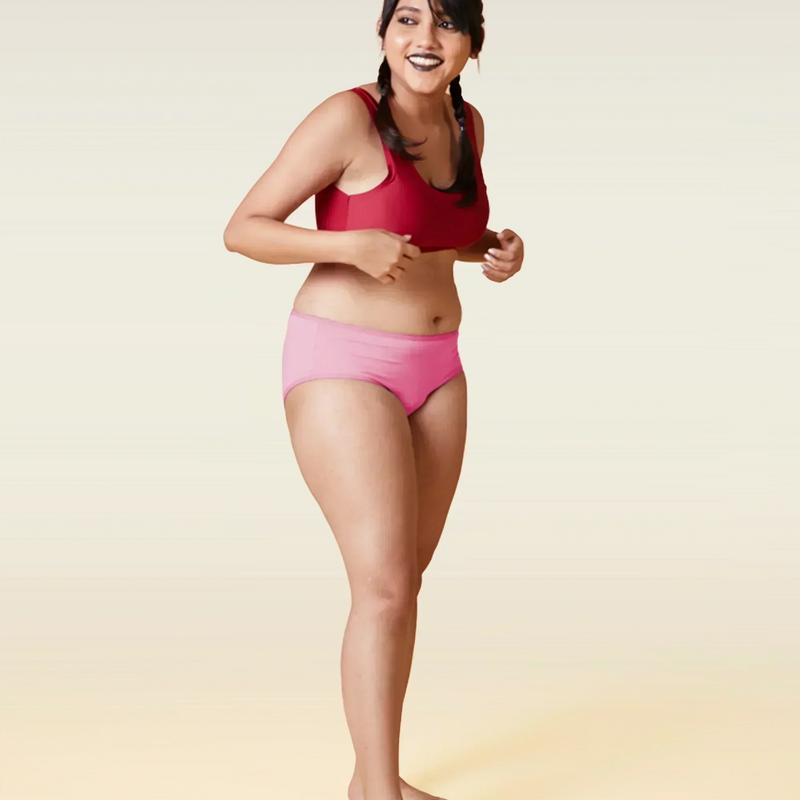 Woman wearing a red sports bra and pink underwear on a beige background