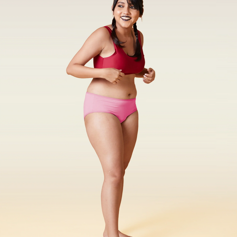 Woman wearing a red sports bra and pink underwear on a beige background