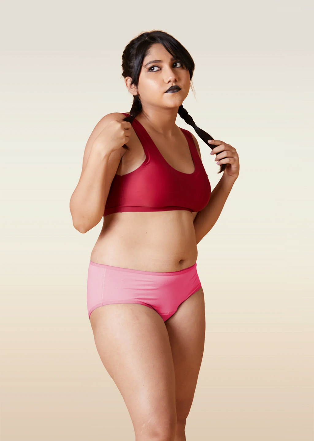 Woman wearing a red sports bra and pink underwear on a beige background