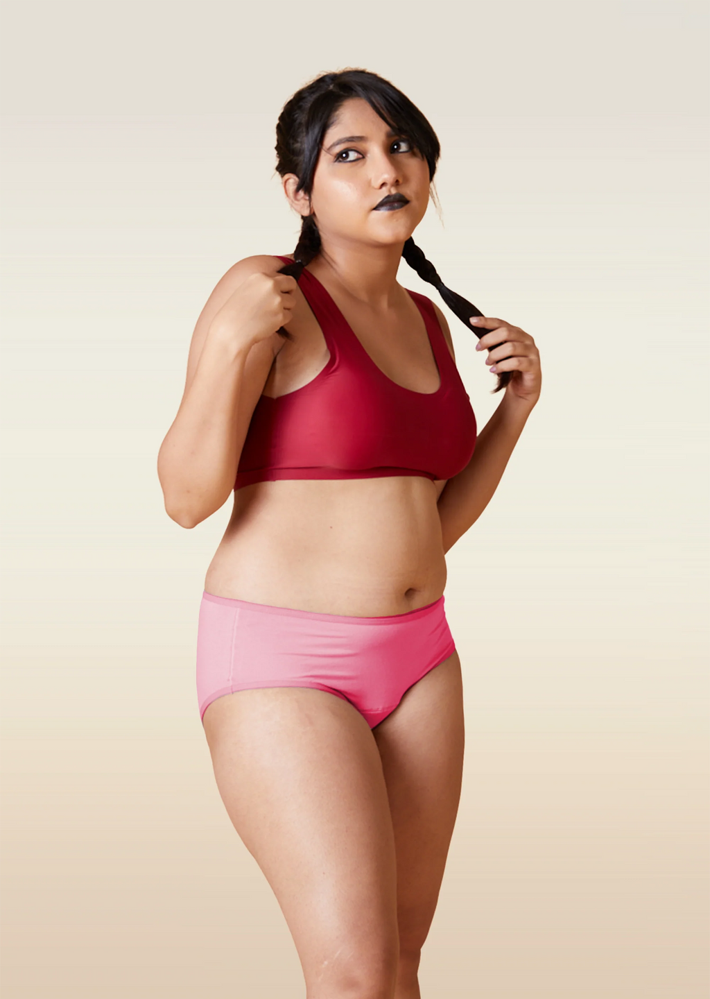 Woman wearing a red sports bra and pink underwear on a beige background