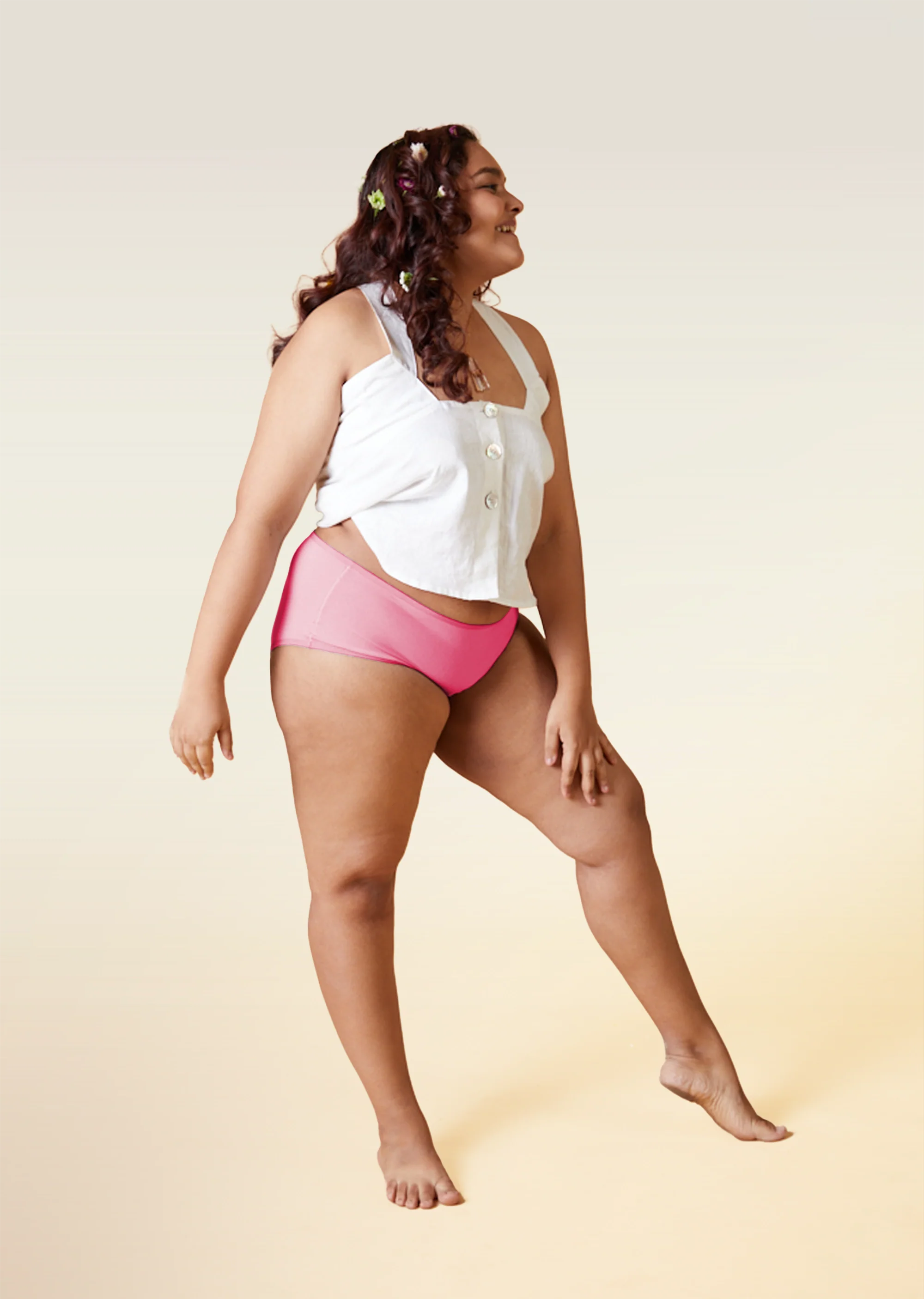 Woman wearing a white top and pink mid-waist underwear on a beige background