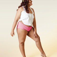 Woman wearing a white top and pink mid-waist underwear on a beige background