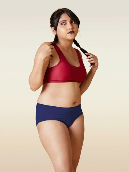 Woman wearing a red sports bra and blue breifs on a beige background