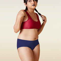 Woman wearing a red sports bra and blue breifs on a beige background