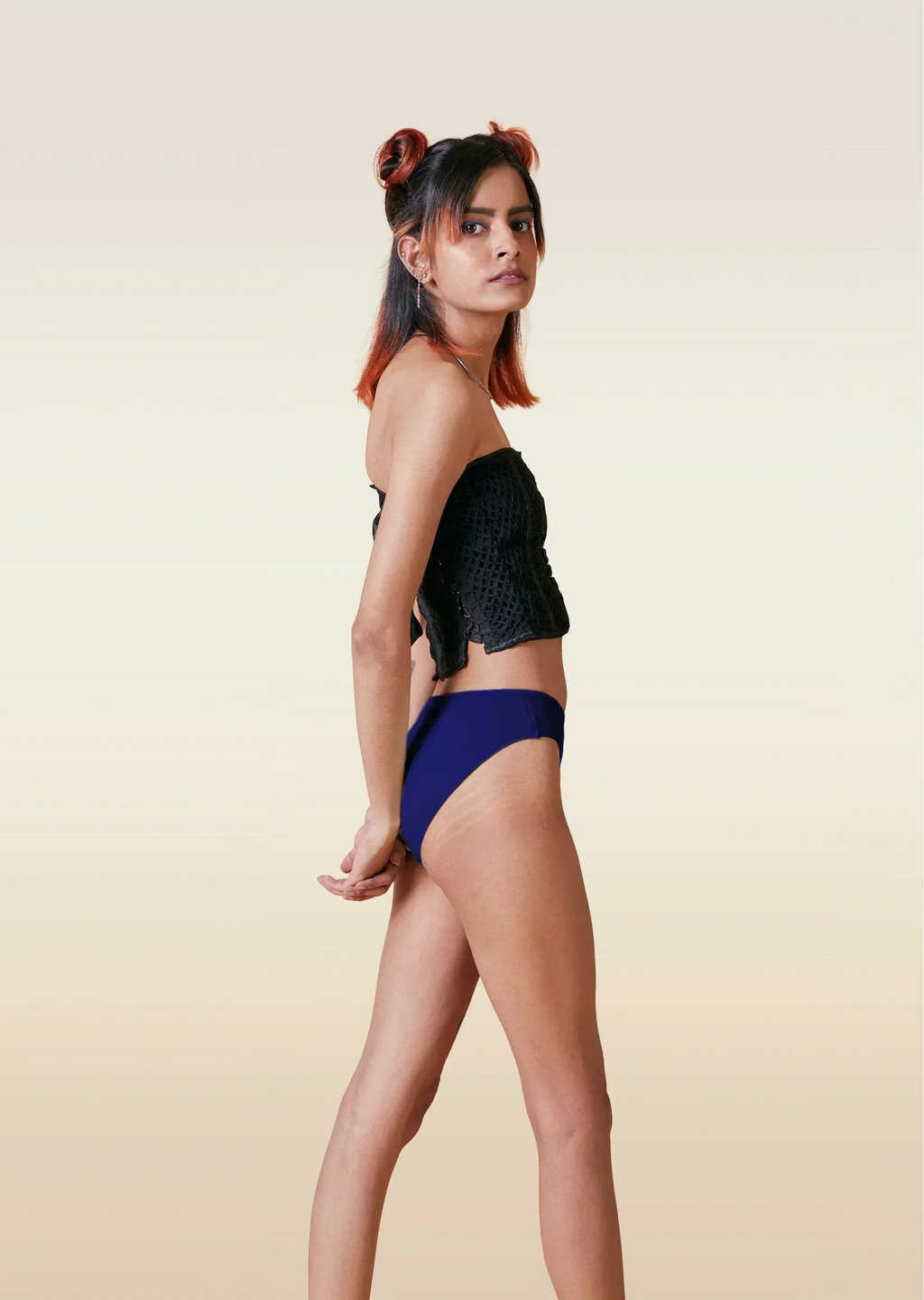 Woman wearing a black bikini top and blue high-waisted bottoms on a beige background