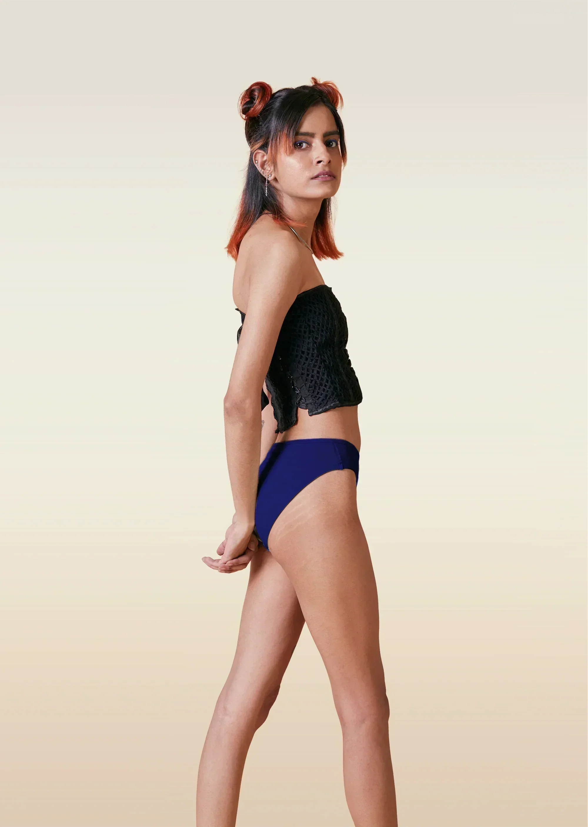 Woman wearing a black bikini top and blue high-waisted bottoms on a beige background