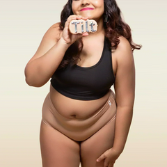 Woman wearing a black tank top and beige mid-waist underwear holding a 'Tilt' sign.