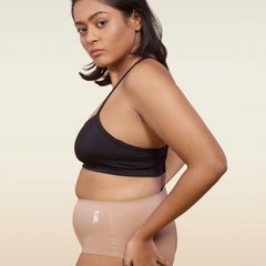 Woman wearing a black sports bra and beige mid-waist underwear on a beige background
