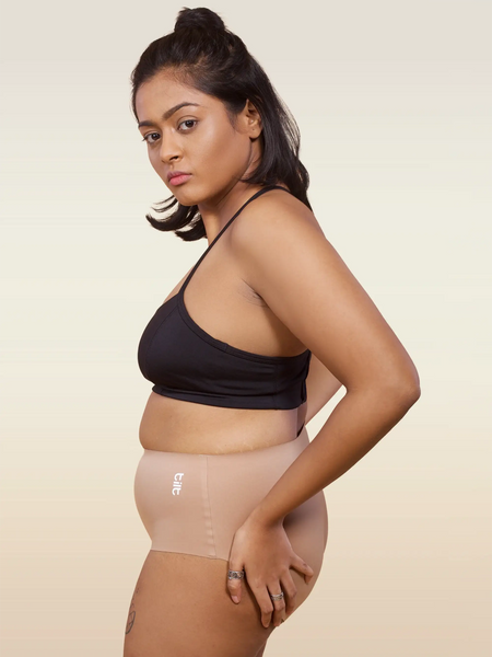 Woman wearing a black sports bra and beige mid-waist underwear on a beige background