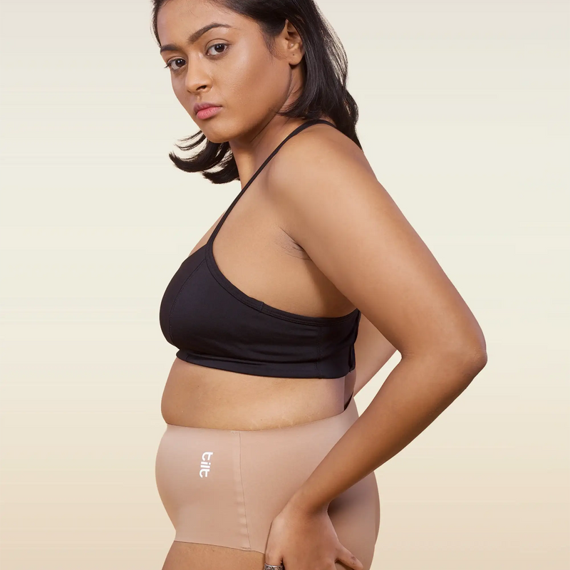 Woman wearing a black sports bra and beige mid-waist underwear on a beige background