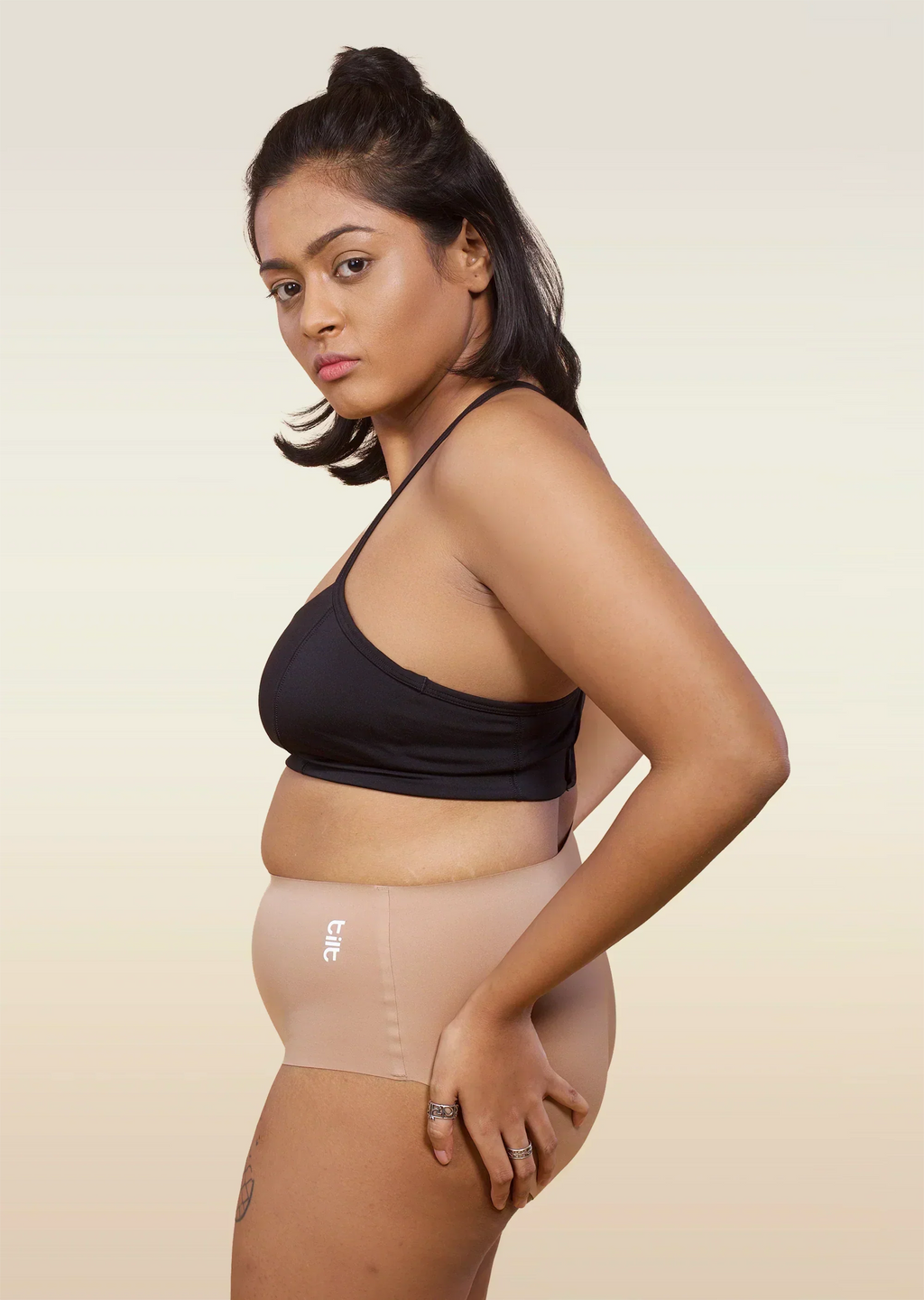 Woman wearing a black sports bra and beige mid-waist underwear on a beige background
