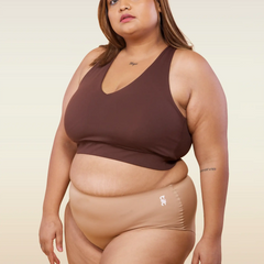 Woman wearing a brown sports bra and beige mid-waist underwear on a beige background