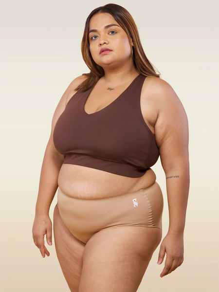 Woman wearing a brown sports bra and beige mid-waist underwear on a beige background
