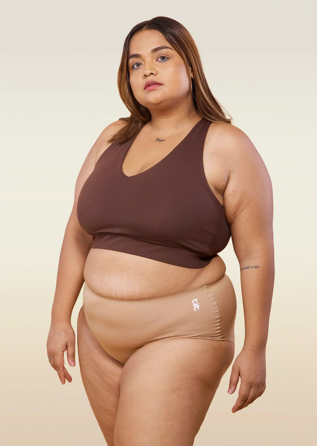 Woman wearing a brown sports bra and beige mid-waist underwear on a beige background