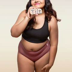 Woman wearing a black tank top and pink mid-waist underwear holding a 'Tilt' sign.