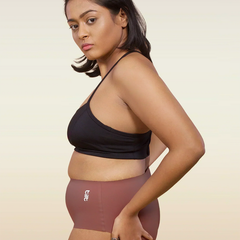 Woman wearing a black sports bra and pink mid-waist underwear on a beige background