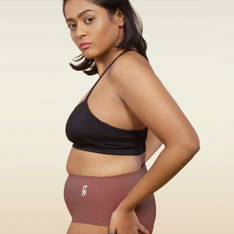 Woman wearing a black sports bra and pink mid-waist underwear on a beige background