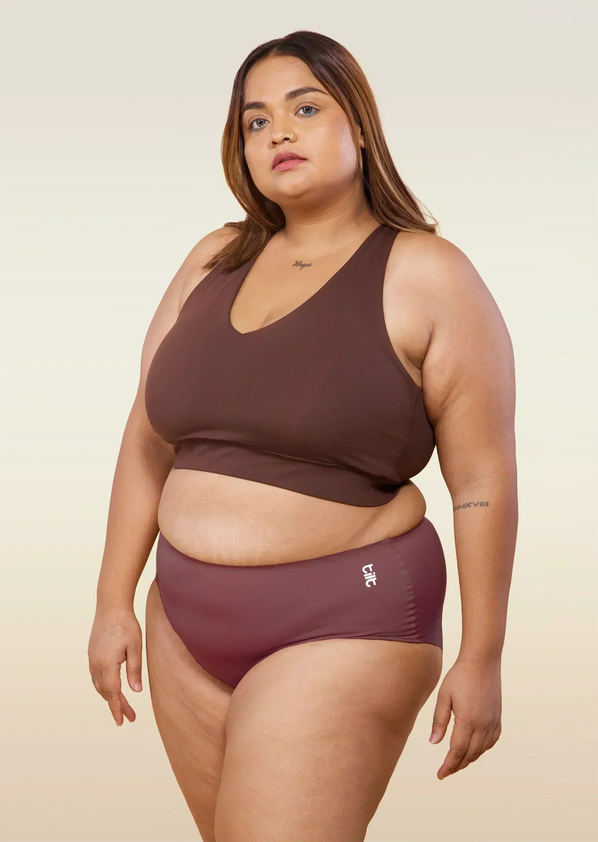 Woman wearing pink underwear and brown sports bra with a beige background