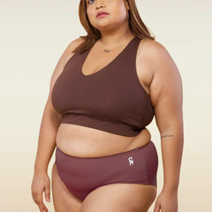 Woman wearing pink underwear and brown sports bra with a beige background